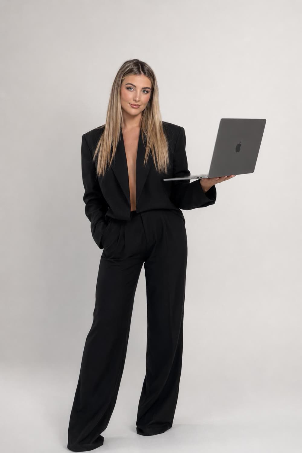 Lourdes de pie con traje negro sosteniendo un portátil en un estudio